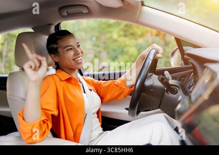 Gioiosa donna nera che balla in macchina, indicando con entusiasmo Foto Stock