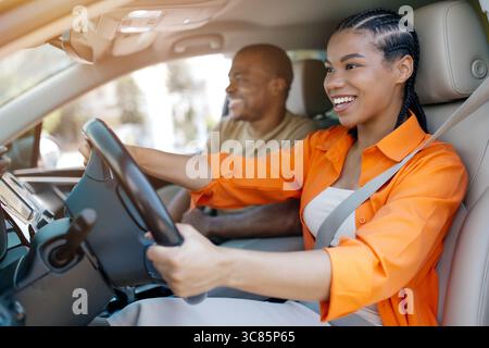 Giovane donna felice che guida un'auto mentre il suo partner si diverte a cavalcare accanto a lei Foto Stock