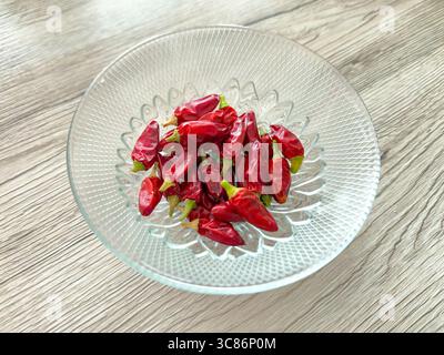 Peperoncini rossi caldi in una ciotola di vetro su una scrivania di legno Foto Stock