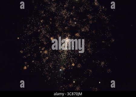 Un colorato spettacolo di fuochi d'artificio illumina il cielo notturno sopra una piccola città durante il festival estivo. Raffiche di luce brillanti creano un atmos festivo Foto Stock