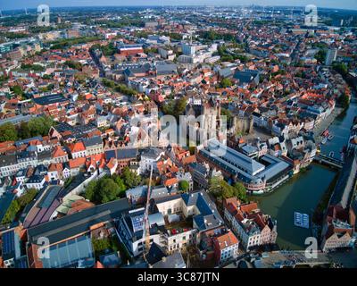 Vista aerea di una città medievale con canali che riflettono il cielo, antichi edifici con tetti di tegole rosse e l'imponente castello di Gravensteen, Gentent e Fiandre. Foto Stock