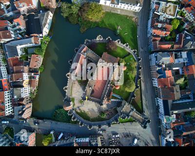 Vista aerea del castello di Gravensteen circondato da un fossato riflettente, che si erge come una fortezza medievale in pietra tra i tetti di tegole rosse della città, Gand, Fiandre, Belgio. Foto Stock