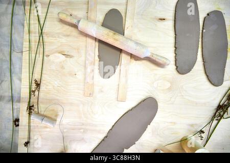 Fogli di argilla laminati disposti su una superficie di legno con un mattarello e utensili da taglio. Un palcoscenico pratico nella realizzazione di anelli per tovaglioli in argilla fatti a mano, dove Foto Stock