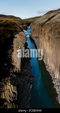 Maestose colonne di basalto si innalzano drammaticamente lungo le acque turchesi del canyon Studlagil in Islanda. I visitatori si meravigliano di fronte a questa meraviglia geologica, creando un'avventura all'aperto mozzafiato. Foto Stock