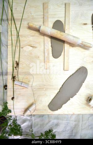 Fogli di argilla laminati disposti su una superficie di legno con un mattarello e utensili da taglio. Un palcoscenico pratico nella realizzazione di anelli per tovaglioli in argilla fatti a mano, dove Foto Stock
