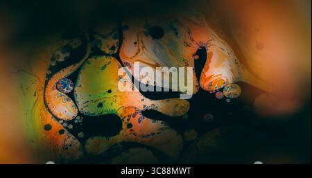 Sfondo dell'inchiostro illuminato. Sfocatura della bolla di vernice. Bagliore di miscela di emulsione di olio su acqua nera. Colore verde arancio astratto, lucentezza fluida, texture artistica. Foto Stock