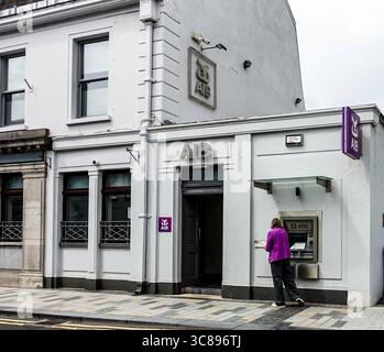 Donna che usa un bancomat fuori dalla filiale della banca AIB a Carrick-on-Shannon, Contea di Leitrim. Strada urbana con segnaletica e facciata in pietra. Foto Stock