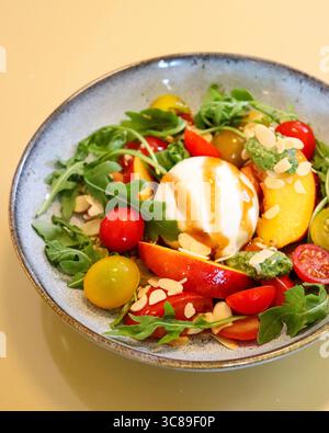 Un'insalata di burrata fresca, con una palla di burrata cremosa posta al centro di un colorato mix di pomodori ciliegini e foglie verdi Foto Stock