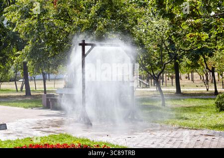 Telaio per irrorazione dell'acqua per il raffreddamento in caso di clima caldo sulla strada cittadina di Kiev, Ucraina. Sistema nebbia di raffreddamento a nebbia d'acqua nel parco cittadino durante la calda estate. Protezione aga Foto Stock