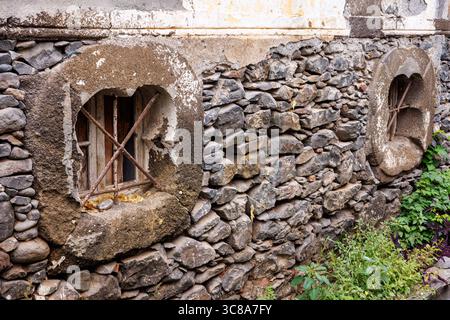 Vecchie finestre nel seminterrato con barre di ferro su un muro di pietra. Vecchie mura in pietra con finestre a figura. Foto di alta qualità Foto Stock