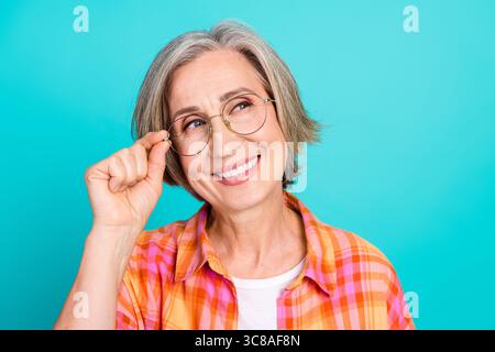 Donna senior sorridente con capelli grigi e occhiali in camicia casual a quadri su sfondo turchese Foto Stock
