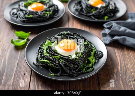 Pasta al nero di calamaro ricoperta da un uovo fritto con il lato del sole, un piatto gourmet di pesce dai sapori ricchi e un fascino visivo unico. Foto Stock