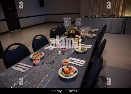 Elegante tavolo da banchetto con insalate, fiori e candele per cena di gala Foto Stock