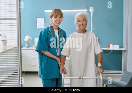 Donna caucasica anziana che usa Walker assistita da giovane infermiera donna adulta sorridente Foto Stock