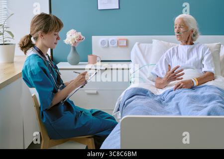 Infermiera donna caucasica intervista donna caucasica anziana giacente nel letto di ospedale Foto Stock