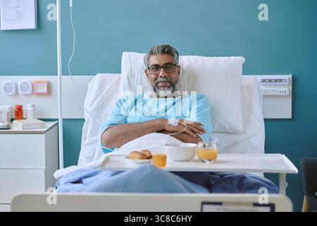 Ritratto dell'uomo birazziale di mezza età che si sta riprendendo nel letto di ospedale dopo l'intervento chirurgico Foto Stock