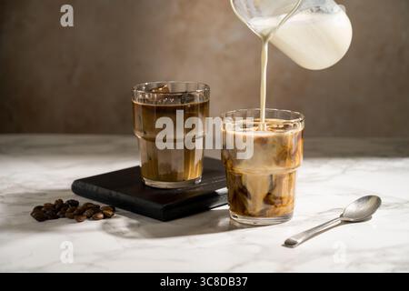 Versare il latte sul bicchiere con il caffè, preparare una bevanda a base di latte ghiacciato Foto Stock