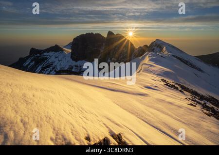 Vista aerea delle maestose vette innevate baciate dalla luce dorata del sole che sorge, illuminando il paesaggio aspro del Monte Kenya, Kenya. Foto Stock