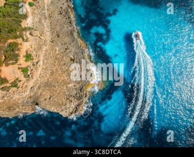 Vista aerea del motoscafo che fa onde vicino alla costa rocciosa Foto Stock