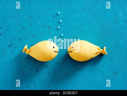 Due palloncini gialli a forma di pesce sono rivolti uno di fronte all'altro su uno sfondo blu con bolle tra di loro, creando una giocosa scena sott'acqua Foto Stock