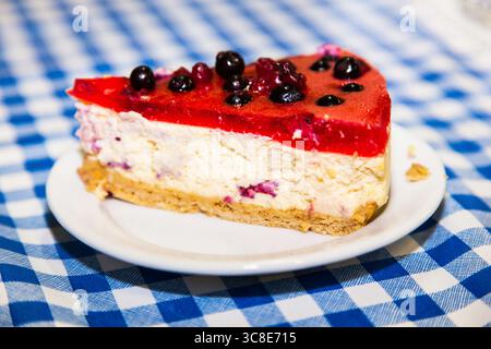 Fetta di torta al formaggio con bacche di ribes nero su un tavolo in un piatto bianco. Foto Stock