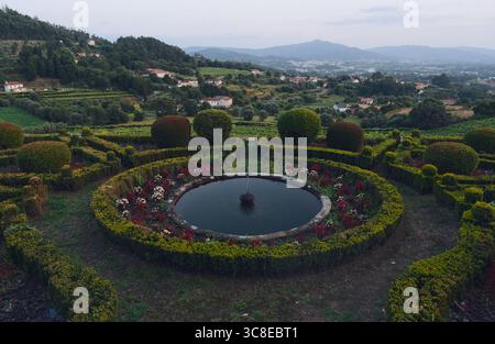 Fontana circolare circondata da fiori vivaci e siepi scolpite nei giardini terrazzati di Paco de Calheiros Foto Stock