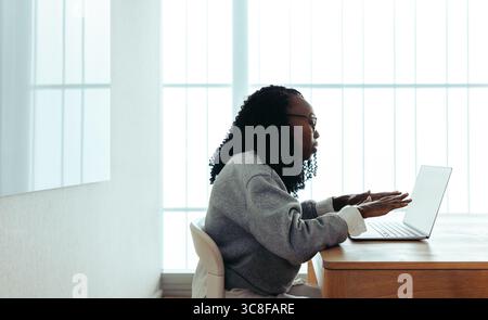 Una donna professionista afroamericana è impegnata a lavorare sul suo laptop, situato in un ufficio contemporaneo. Questa immagine cattura l'essenza della messa a fuoco, produ Foto Stock