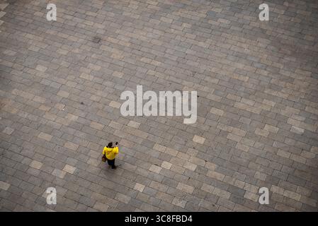 Persona in giacca gialla che cammina attraverso la piazza lastricata di pietra, vista aerea Foto Stock
