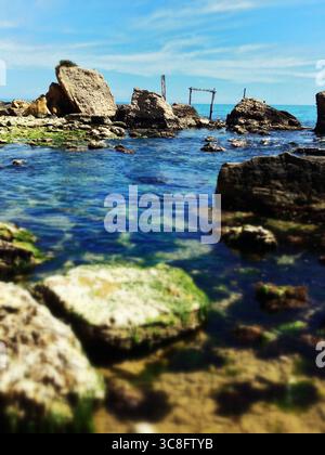 Rocce e pali di legno di un trabocco, una tradizionale macchina da pesca, parzialmente sommersa nel mare Adriatico vicino a Ortona, Abruzzo, Italia Foto Stock