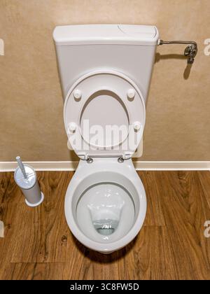 Ciotola bianca con coperchio aperto e vasca a filo su parete marrone e pavimento in legno, vista dall'alto Foto Stock