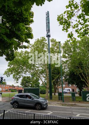 Un'auto passa davanti a un albero di comunicazione 5G per telefoni cellulari, Chingford, Londra, Regno Unito - moderna infrastruttura di telecomunicazione in un ambiente periferico Foto Stock