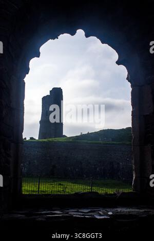 Ammira la solitaria torre spezzata delle rovine del castello di Aberystwyth attraverso una porta del vecchio muro. Il castello originale di Aberstwyth fu costruito da Foto Stock