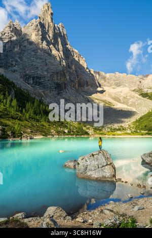 Escursionista donna in piedi sulla roccia, godendo di una vista mozzafiato del Lago Sorapis e delle montagne dolomitiche circostanti nell'Italia settentrionale. Vista posteriore, traslazione, nat Foto Stock