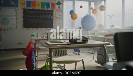 Insegnante donna che posiziona fogli di carta con attività di scrittura sulle scrivanie degli studenti prima della lezione. Spazio per la preparazione degli insegnanti per la lezione o il test scolastico in aula. Donna che lavora nella scuola elementare moderna. Foto Stock