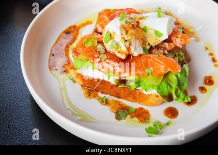 Un delizioso piatto gourmet con un panino a vista di salmone affumicato ricoperto da un uovo perfettamente in camicia e guarnito con lattuga e condimento Foto Stock