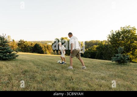 Padre e figlio si divertono con una partita di calcio amichevole in un campo erboso panoramico Foto Stock