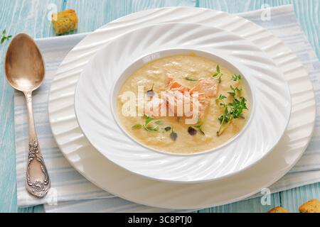 Bisque au saumon, zuppa panna con salmone ed erbe aromatiche in una ciotola bianca su un tavolo di legno turchese con cucchiaio, vista orizzontale, primo piano, non generato dall'IA Foto Stock