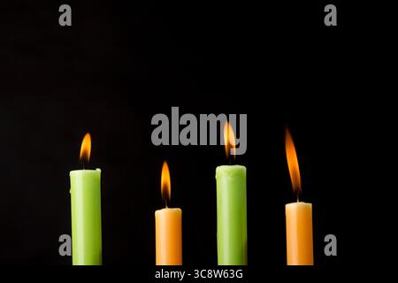 Quattro candele colorate bruciate su sfondo nero. Foto Stock