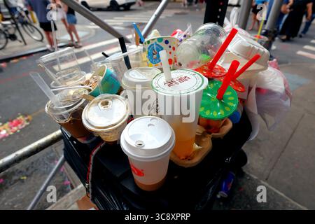 Tazze di plastica monouso, contenitori per alimenti e cannucce posizionate in cima a un cestino privato di un'azienda all'angolo di una strada a New York. Foto Stock