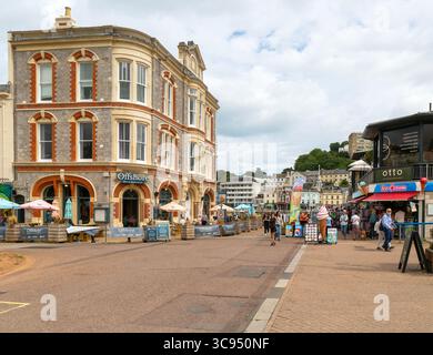 Bar e ristorante offshore, persone che camminano vicino ai negozi sulla banchina, Vaughan Parade, Torquay, Devon, Inghilterra, REGNO UNITO Foto Stock