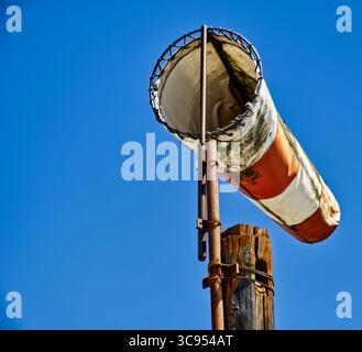 Giacca a vento con strisce arancioni e bianche che si snodano su un palo arrugginito, segnalando la direzione del vento sotto il cielo nuvoloso Foto Stock