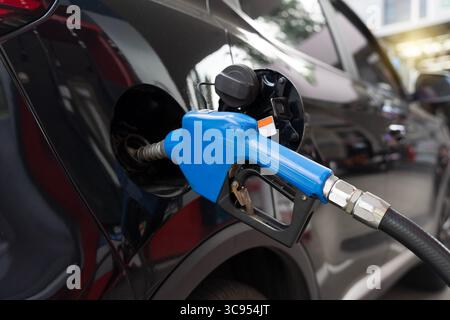 Primo piano di un ugello blu che pompa benzina in un'auto nera presso una stazione di servizio. Concetto di energia di trasporto, rifornimento, costo della benzina e a. Foto Stock