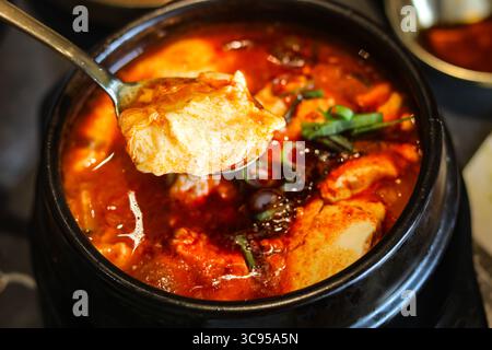 Mangiando Sundubu-jjigae, l'amato stufato coreano di tofu morbido, servito in un tradizionale pentola di terracotta nera. Foto Stock