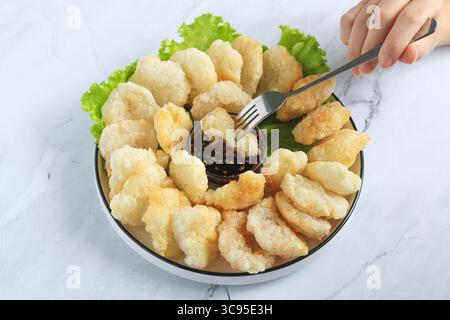 Persona che tiene la forchetta per mangiare il Cireng, un popolare spuntino indonesiano a base di farina di tapioca, organizzato su un piatto bianco. Al centro c'è una salsa subacquea. Foto Stock