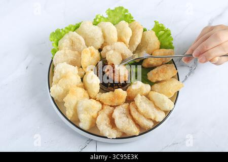 Persona che tiene la forchetta per mangiare il Cireng, un popolare spuntino indonesiano a base di farina di tapioca, organizzato su un piatto bianco. Al centro c'è una salsa subacquea. Foto Stock