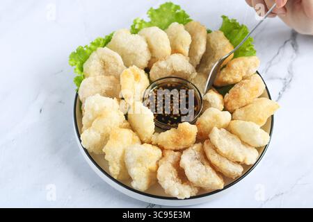 Persona che usa la forchetta per mangiare il Cireng, un popolare spuntino indonesiano a base di farina di tapioca, ordinato su un piatto bianco. Accanto c'è una salsa per immersione. Foto Stock