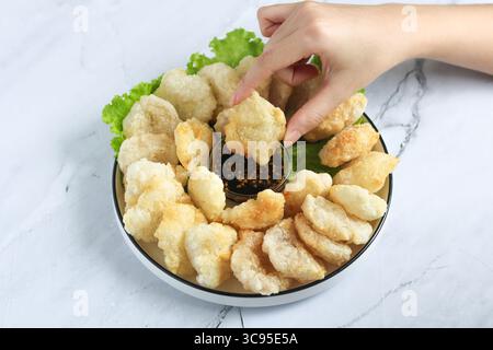 Persona che usa la mano per mangiare il Cireng, un popolare spuntino indonesiano a base di farina di tapioca, ordinato su un piatto bianco. Accanto c'è una salsa per immersione. Foto Stock