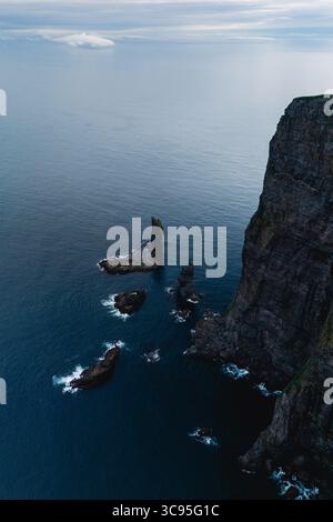 Le maestose scogliere si innalzano drammaticamente dalle tranquille acque atlantiche delle Isole Faroe, adornate da formazioni rocciose uniche. Scogliere Risin OG Kellingin Foto Stock