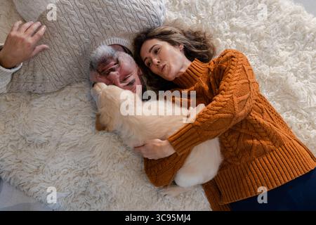Una coppia che indossa maglioni in maglia su un tappeto bianco sporco a casa coccolando il cucciolo Golden retriever Foto Stock