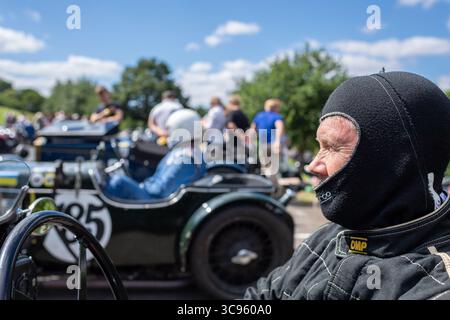 Uomo che indossa tute ignifughe e una balaclava nel paddock durante una gara VSCC in preparazione alla gara. Foto Stock